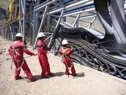 Three fitters in red overalls and hard hats pulling a new belt into a conveyor structure.