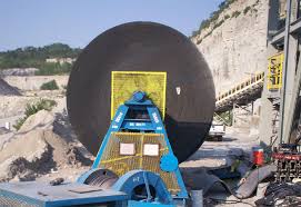 A large belt roll standing on a handling frame at a quarry, with the conveyor it is being fitted to behind it.