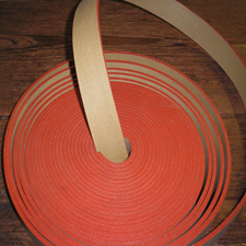 A coil of red rubber transmission belting with one end lifted away from the roll. A coil of red rubber transmission belting with one end lifted away from the roll.