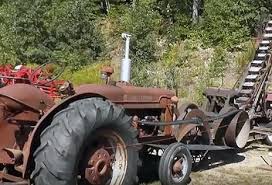 A farm tractor parked beside a machine it drives by a long flat belt. A farm tractor parked beside a machine it drives by a long flat belt.