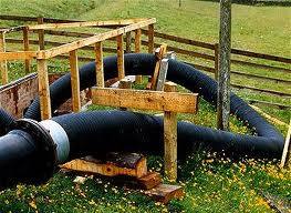 A large bore suction hose running over a timber trestle in a field to the pipeline beyond. A large bore suction hose running over a timber trestle in a field to the pipeline beyond.