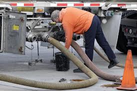 A man in high visibility clothing coupling a hose to a road tanker to unload it. A man in high visibility clothing coupling a hose to a road tanker to unload it.