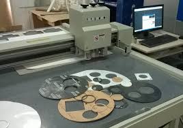 A cutting table with gaskets being cut from rubber sheet under a computer controlled head. A cutting table with gaskets being cut from rubber sheet under a computer controlled head.