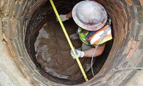 A worker in a harness and hard hat lining the inside of a manhole shaft. A worker in a harness and hard hat lining the inside of a manhole shaft.
